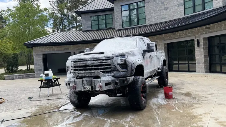 Lifted pickup truck covered in foam during a LabShine mobile wash in front of a garage