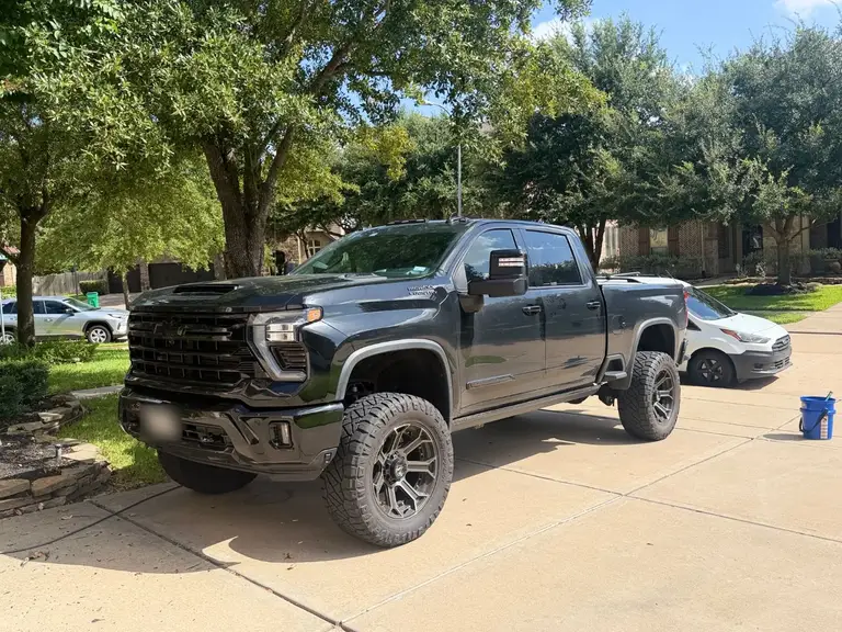 Before: the same lifted Chevrolet Silverado 2500 HD covered in road dust, in the same driveway
